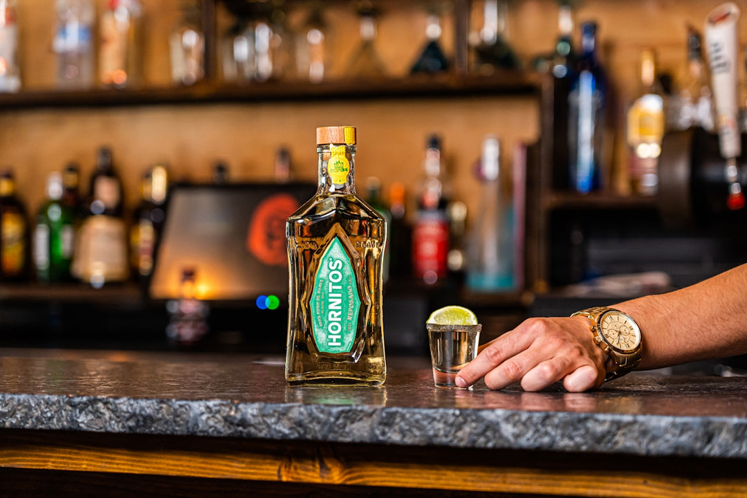 a man holding a bottle of liquor next to a shot glass