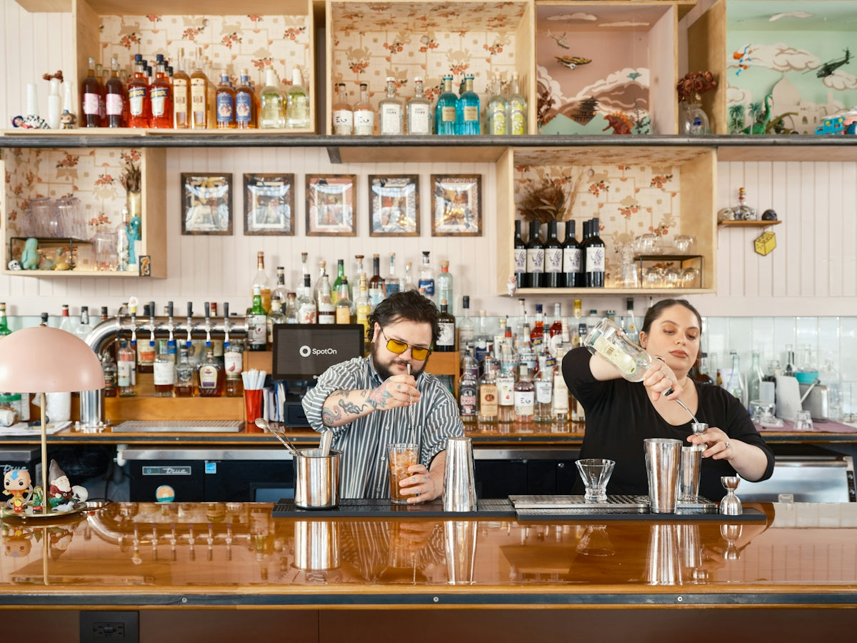 Two bartenders prepare cocktails behind a well-stocked bar.